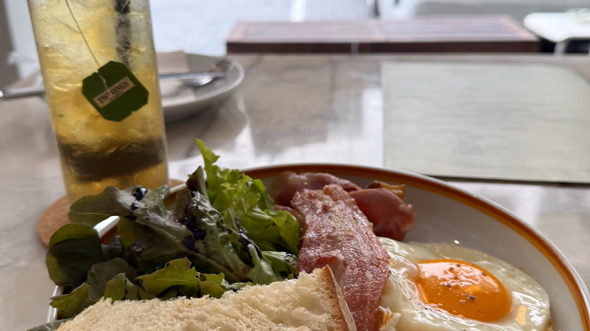 A breakfast plate with sunny-side-up eggs, bacon, and sourdough by a window.