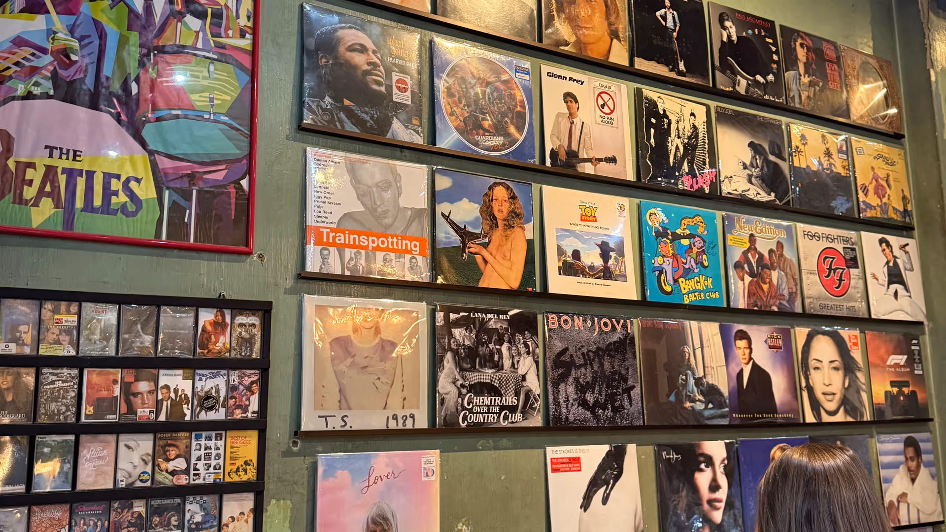 A woman browsing a record store with walls covered in classic vinyl albums.