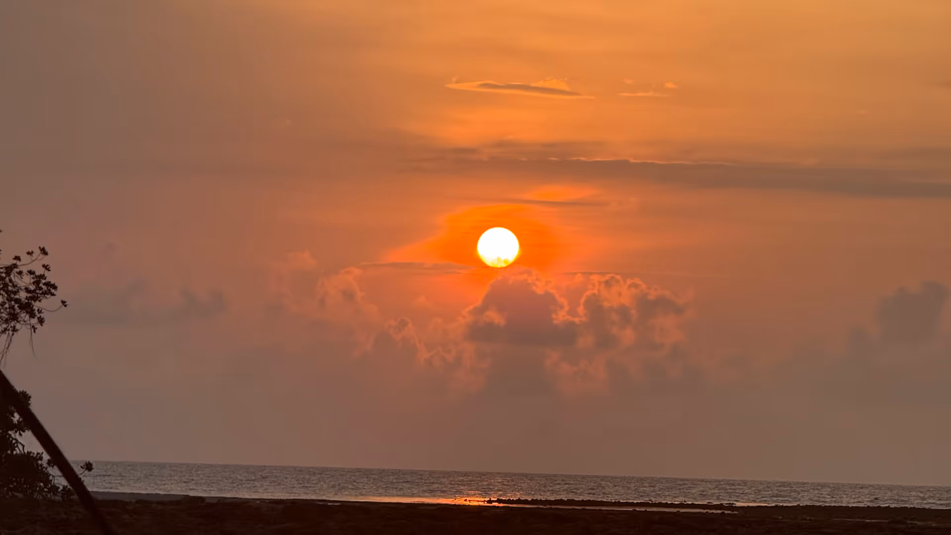The sun breaking over a calm, orange-lit beach during low tide.
