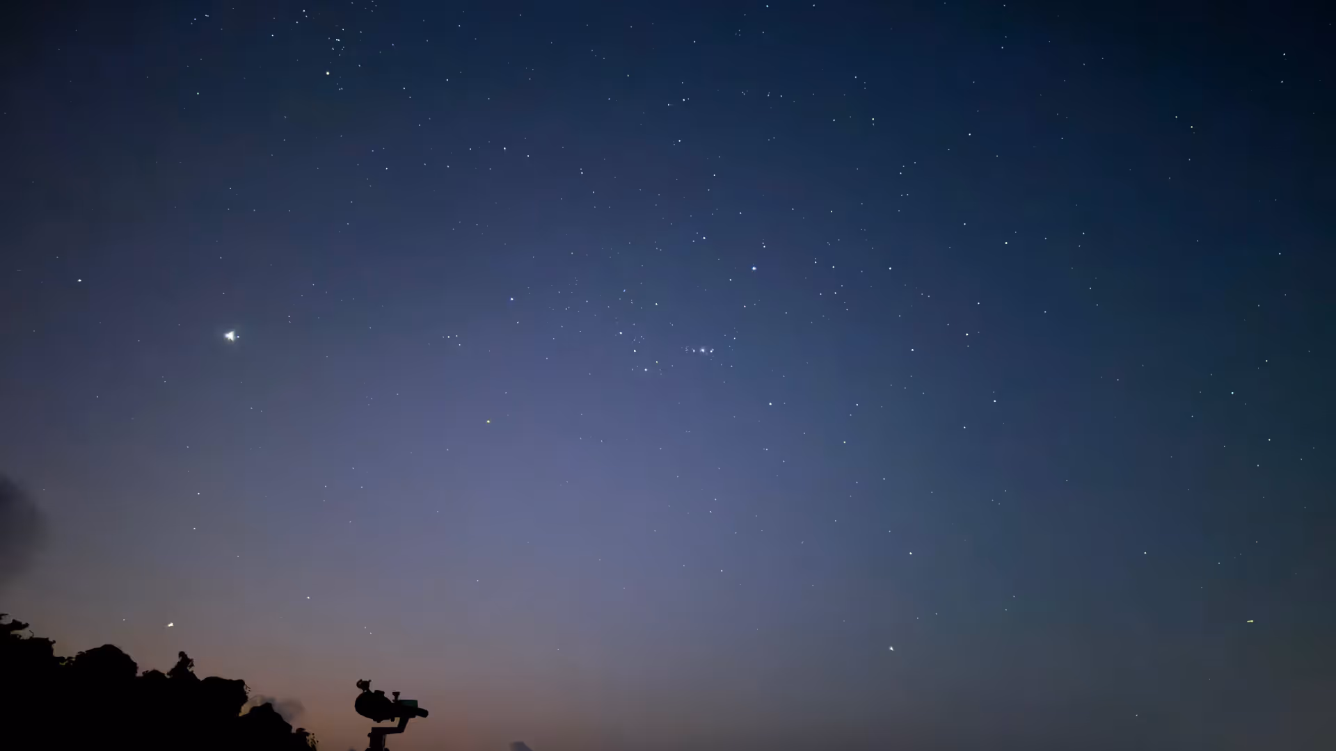 A silhouette of a telescope on a tripod set up on the sand against a starry night sky.