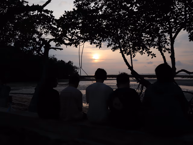 Silhouettes of five friends sitting together on a low wall
