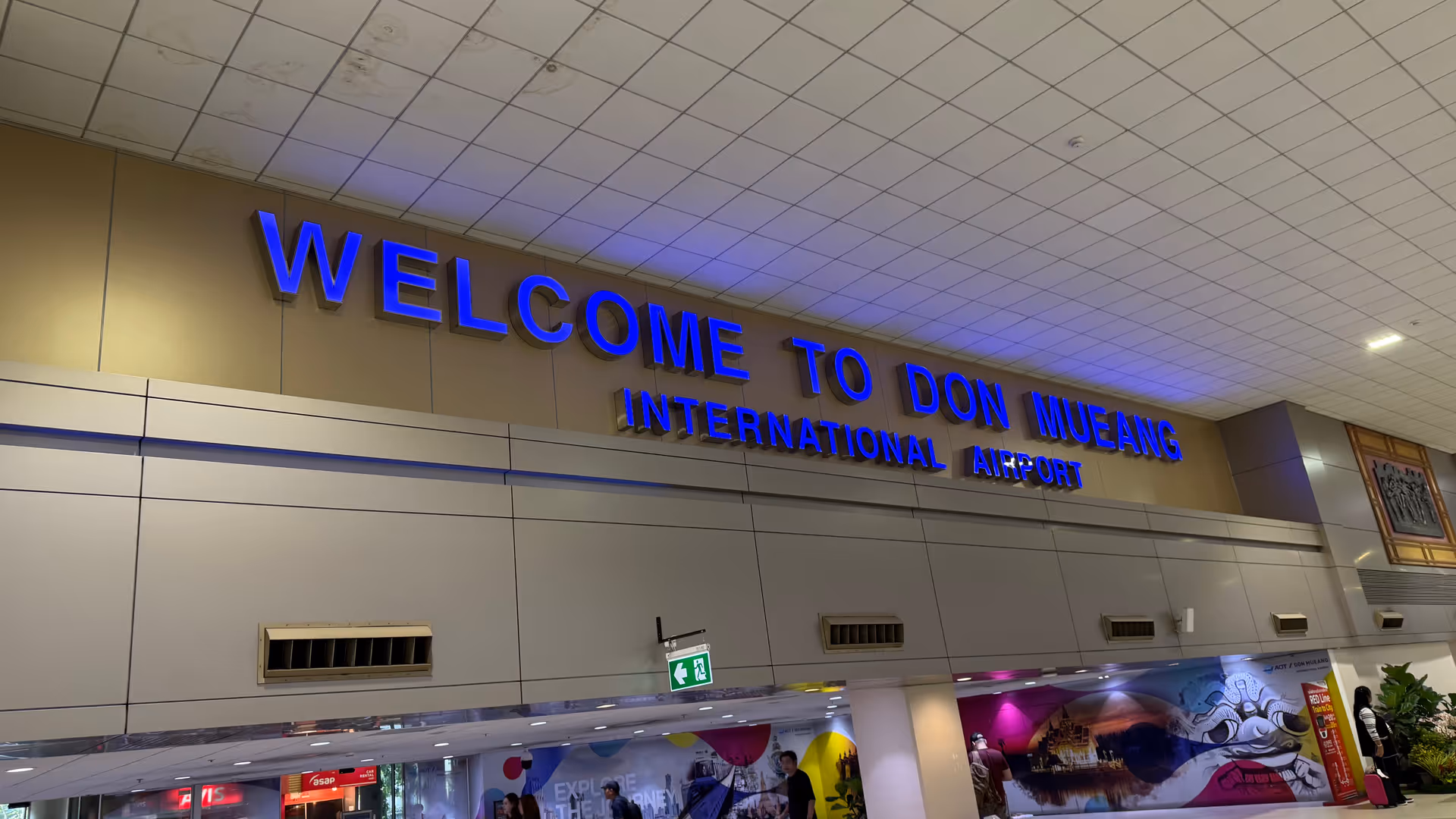 The blue neon 'Welcome to Don Mueang International Airport' sign in the arrival hall.