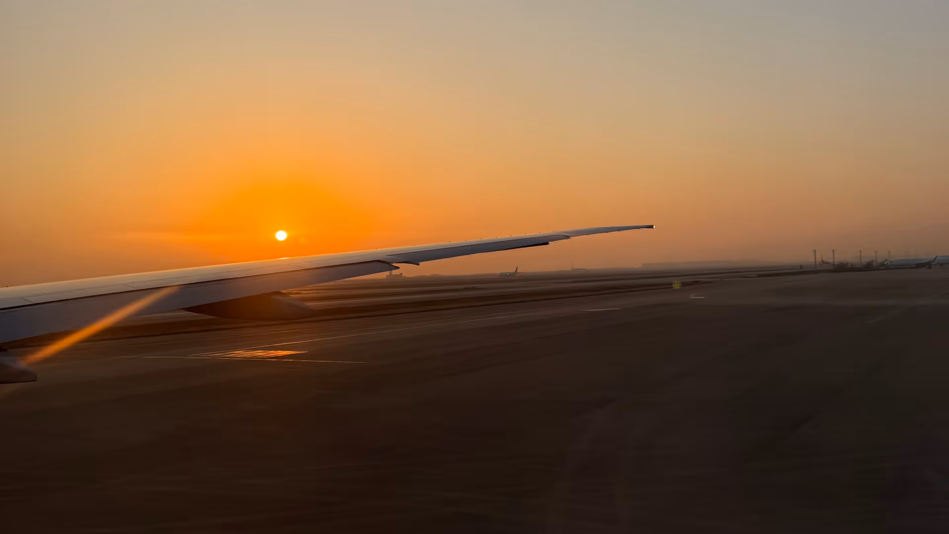 An airplane wing cutting through thick morning fog at Shanghai, a pale orange sunrise barely visible on the horizon.
