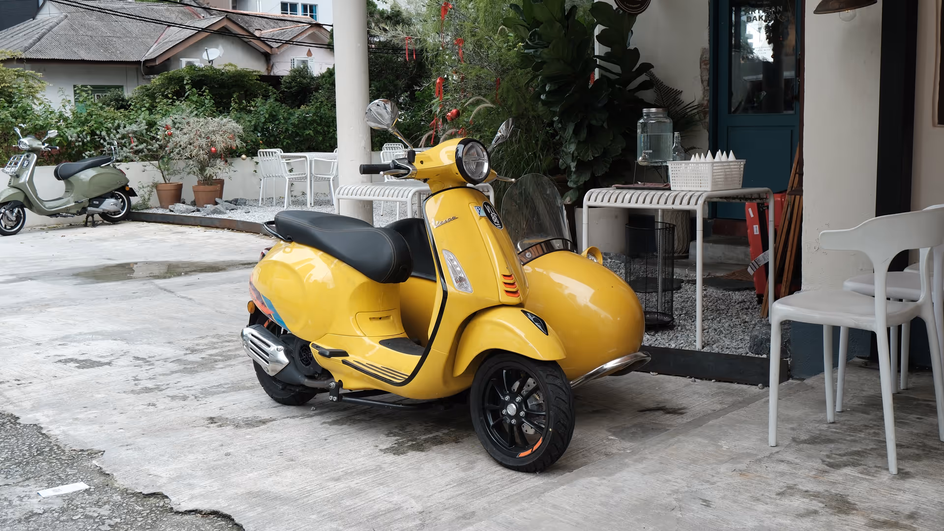 A bright yellow Vespa GTS parked outside Grumpy Bagels, with a second grey Vespa visible in the background.