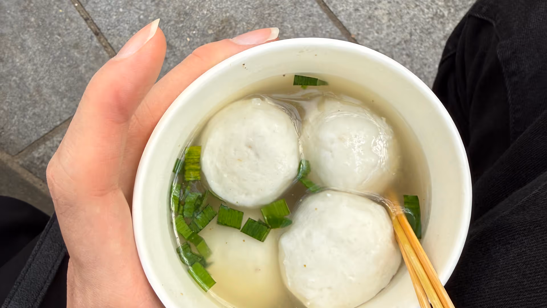 A paper cup of fish ball soup with spring onions, held in hand on the streets of Gulangyu.