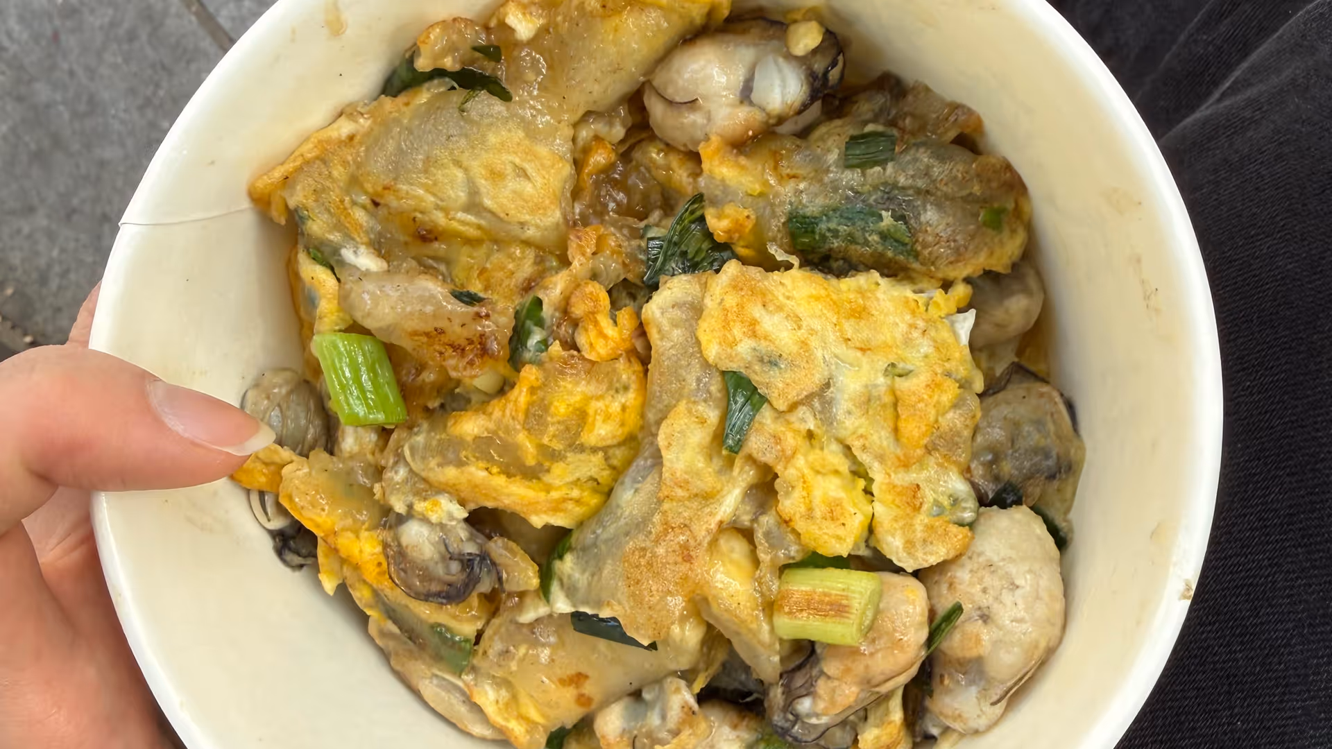 A bowl of oyster omelette with egg and spring onions, held in hand at a Gulangyu street stall.