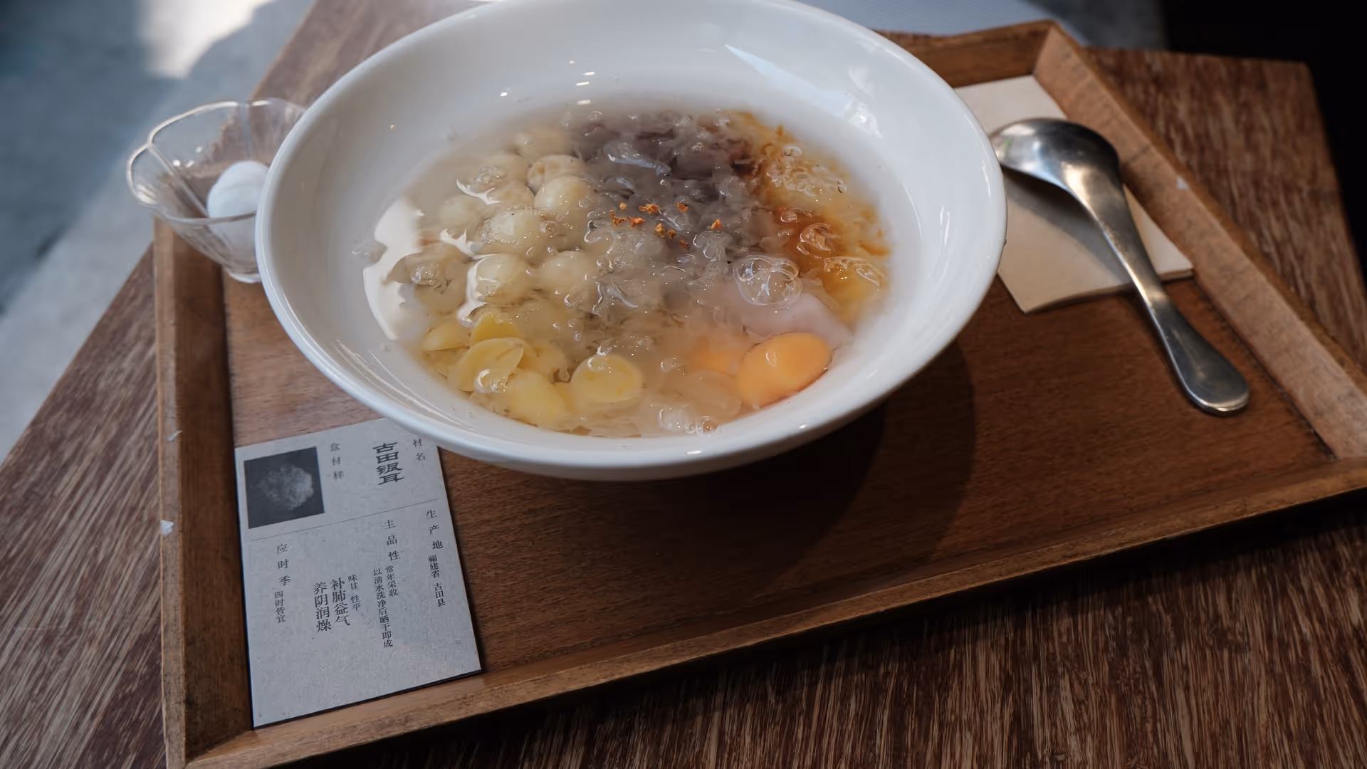 A white bowl of taro dessert with longan and jelly served on a wooden tray at a Gulangyu café.
