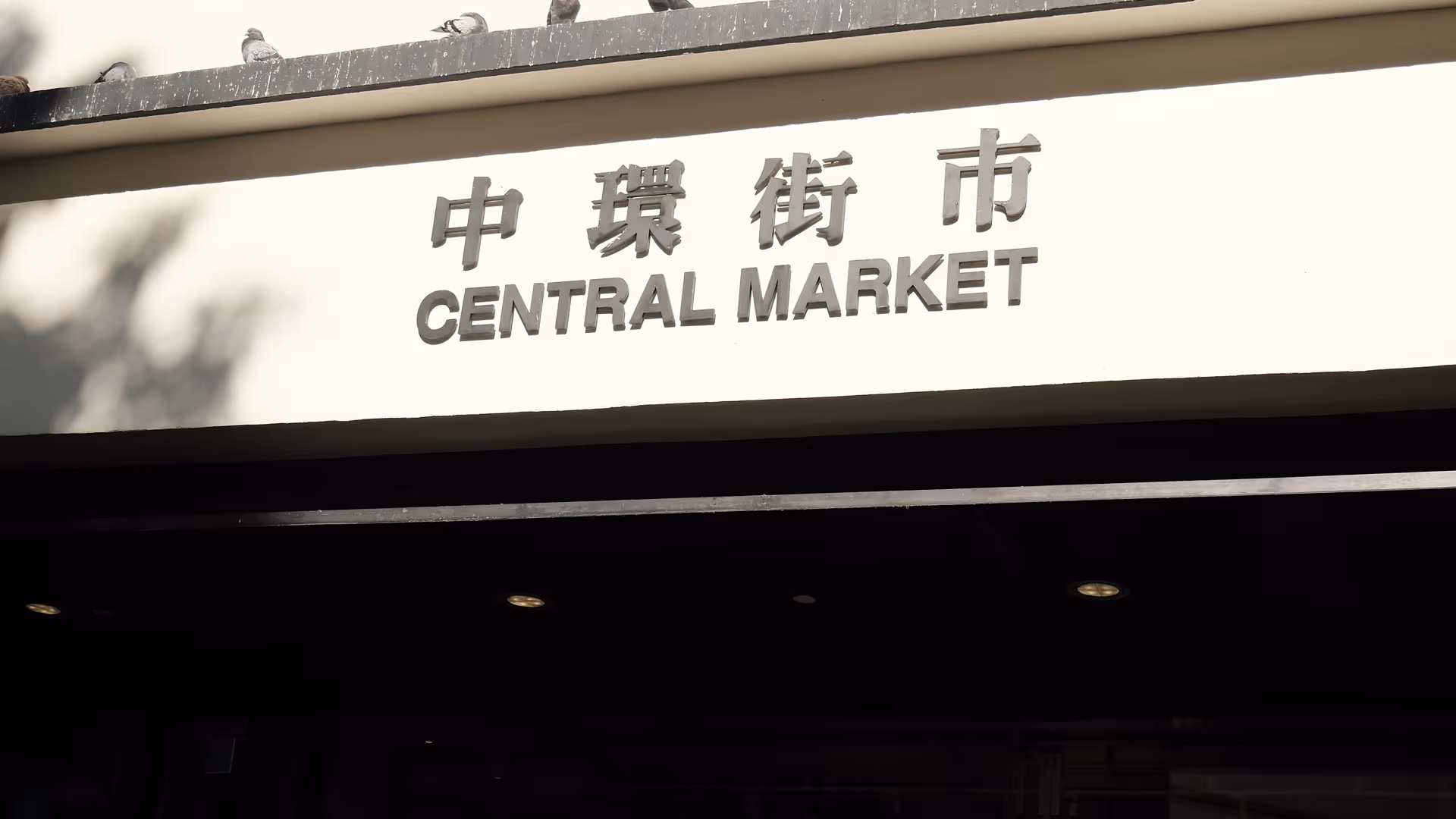 The Central Market entrance sign in English and Chinese, shot from above with pedestrians below.