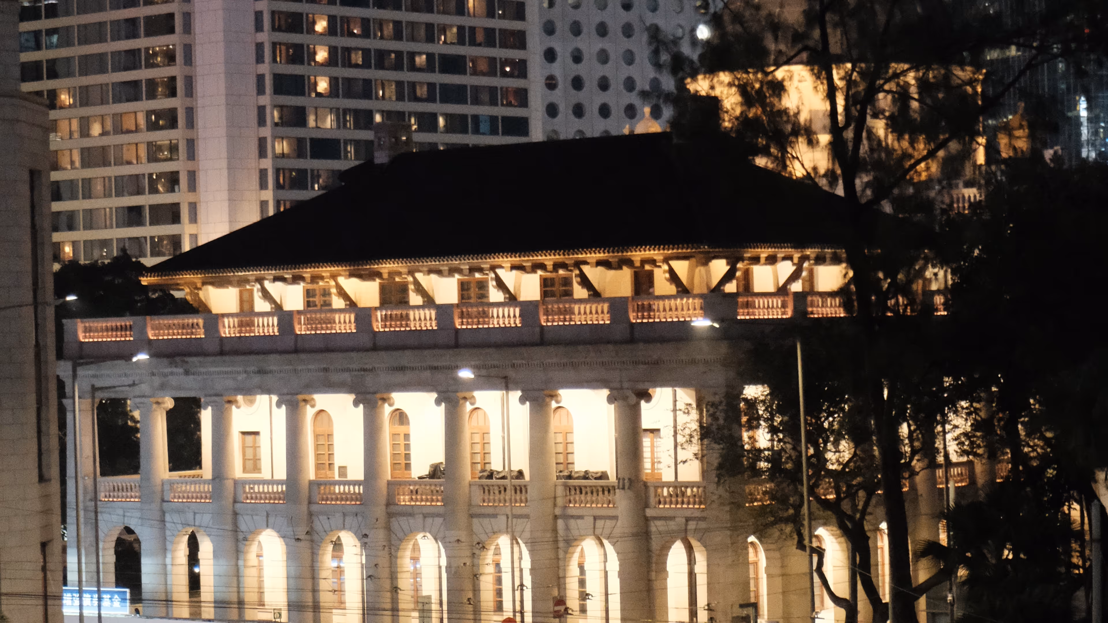 A tram curving past the illuminated Court of Final Appeal building at night in Central Hong Kong.
