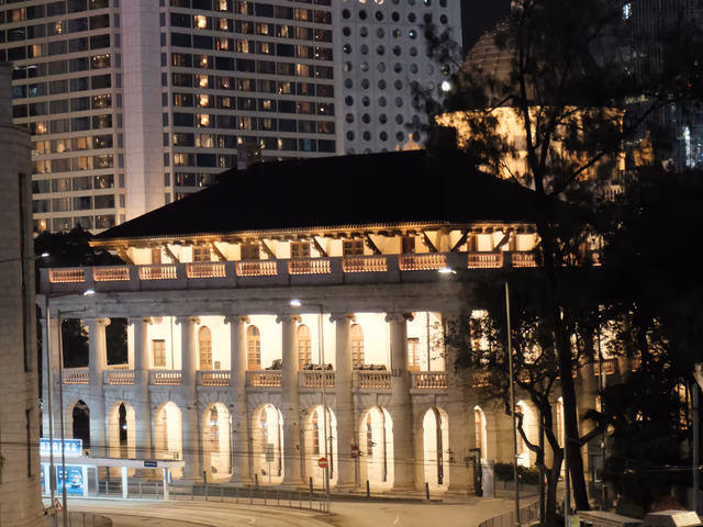 A tram curving past the illuminated Court of Final Appeal building at night in Central Hong Kong.