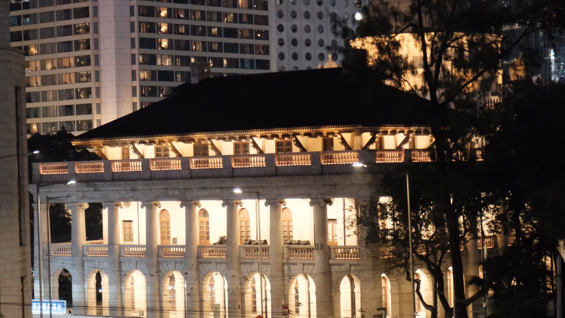 A tram curving past the illuminated Court of Final Appeal building at night in Central Hong Kong.