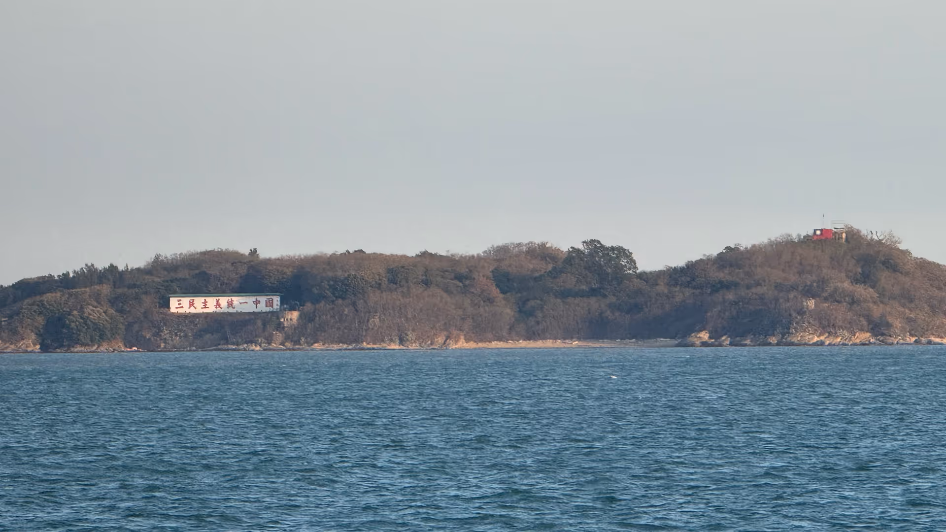 Kinmen Island seen from the boat, a rocky coastline with large Chinese propaganda slogans painted on the hillside.