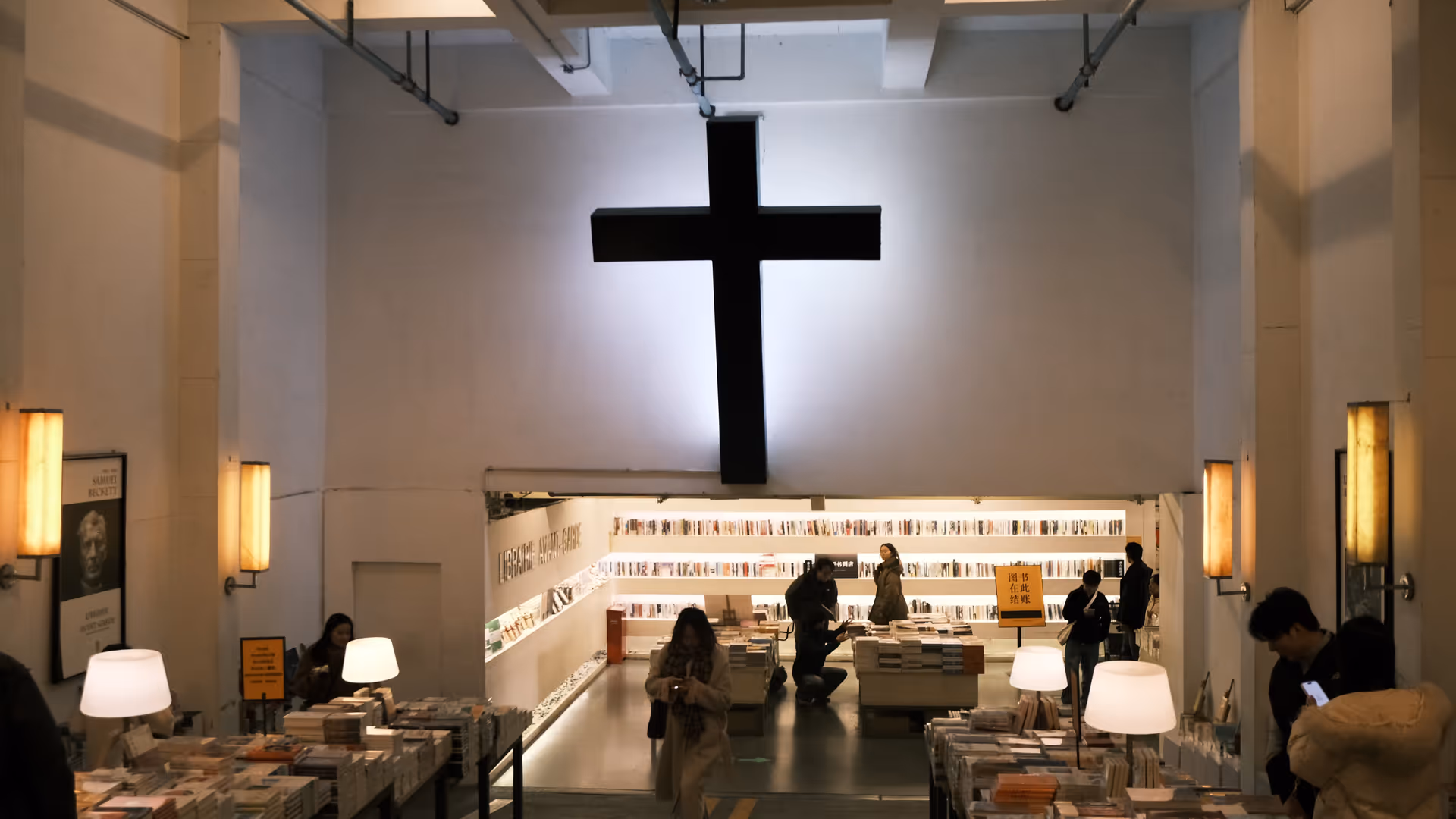 The interior of Librairie Avant-Garde bookshop, a large black cross mounted on a glowing white wall above shelves of books.