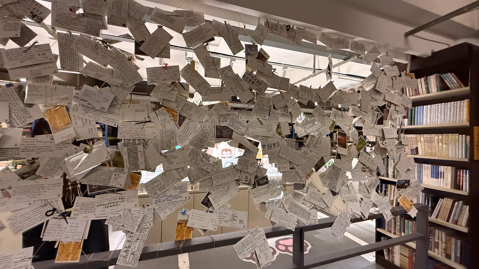 Hundreds of small handwritten notes hanging from wires in a cloud-like installation at Librairie Avant-Garde.