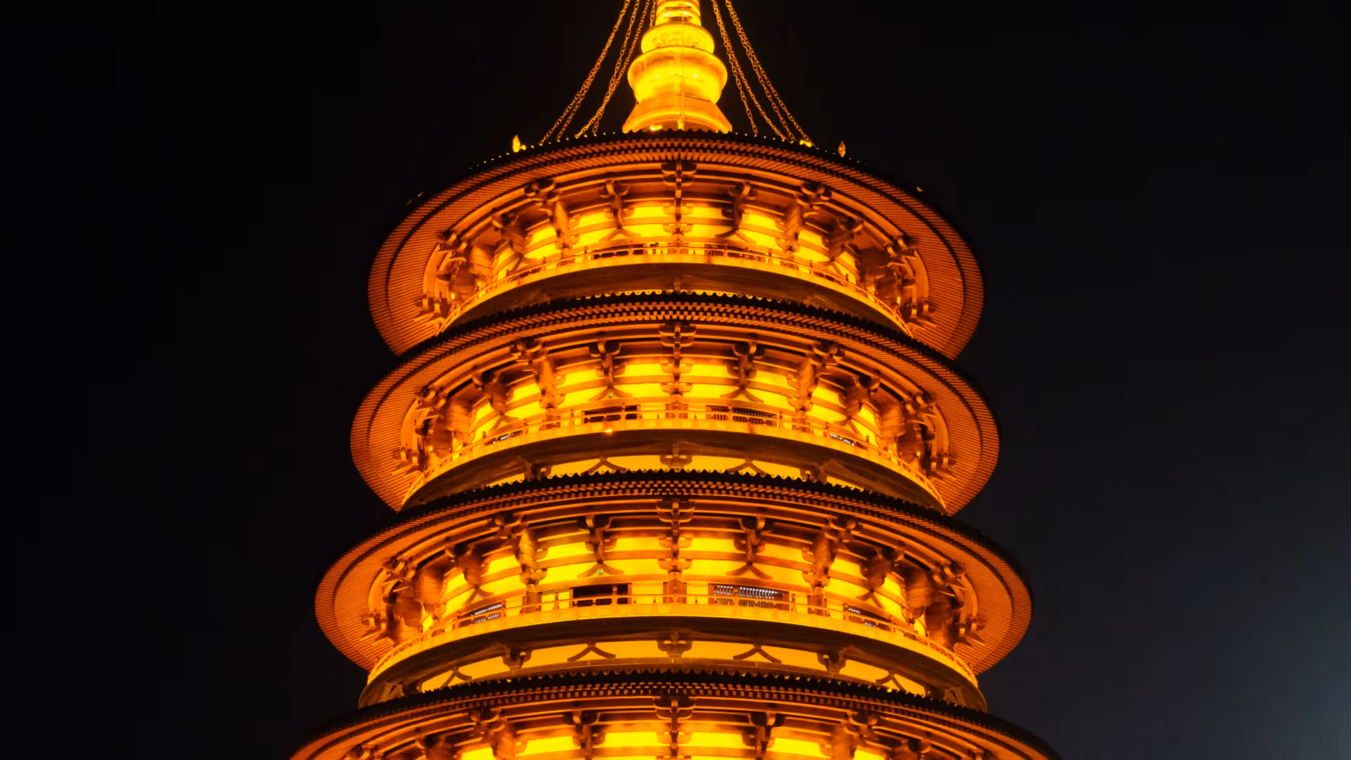 A multi-tiered Chinese pagoda lit up in glowing amber rings against a pitch black night sky in Luoyang.