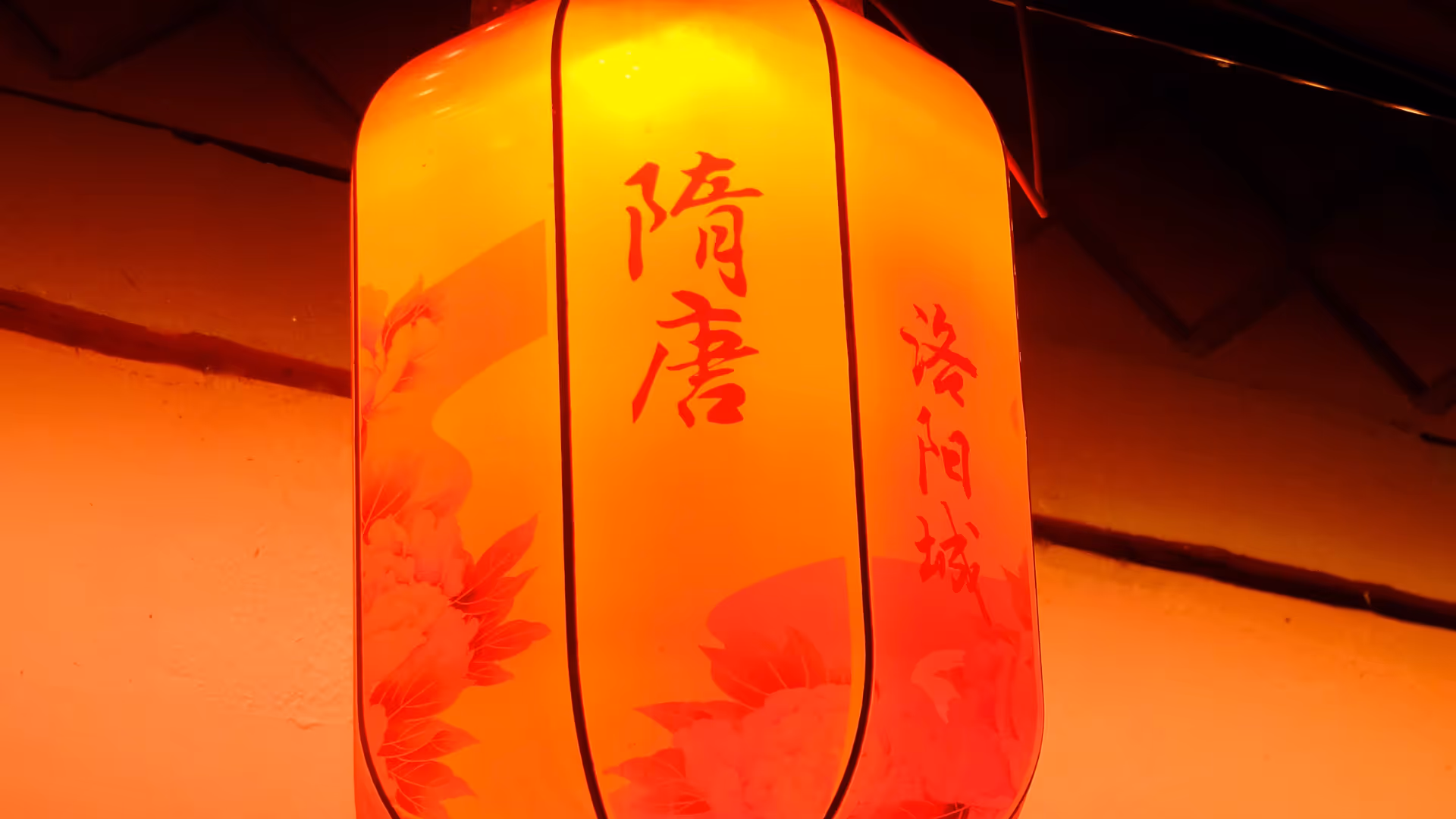 A red paper lantern with Chinese characters hanging from a dark rooftop in Luoyang at night.
