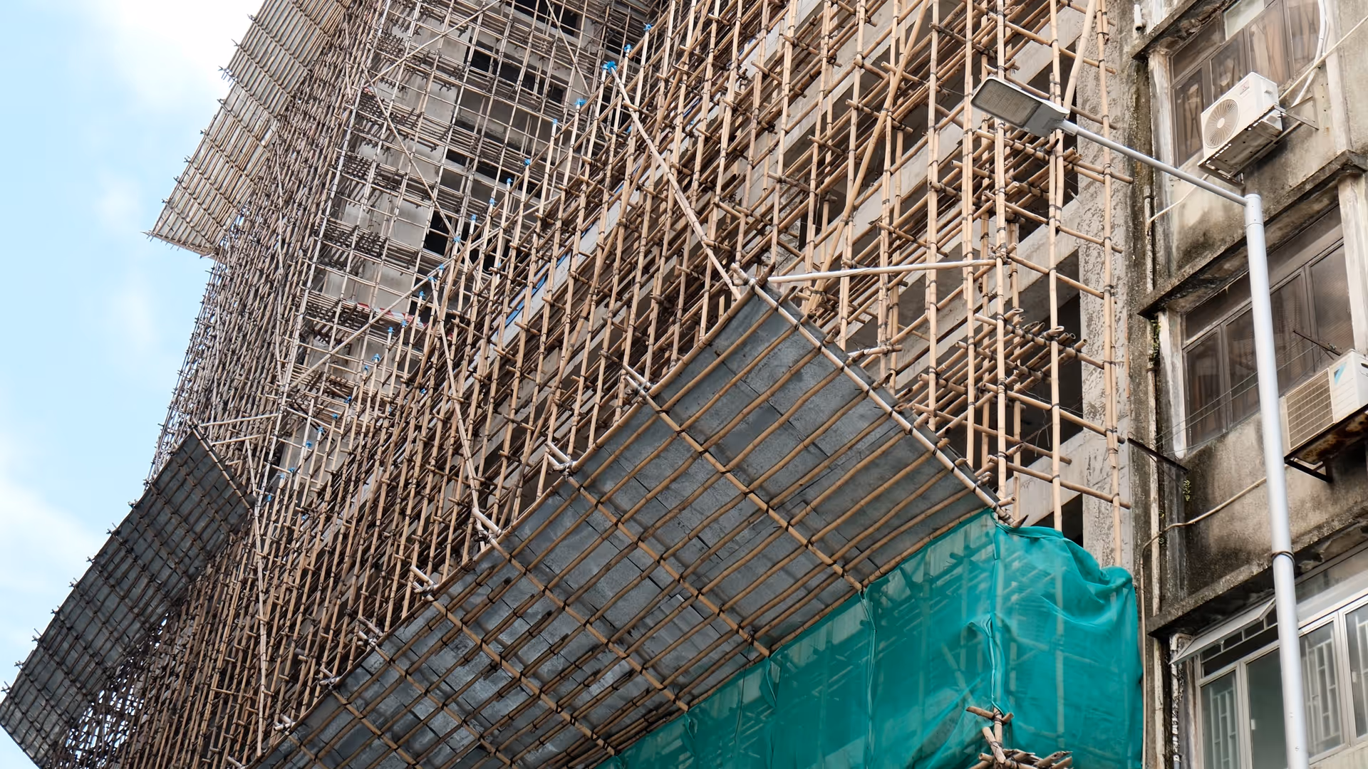A building facade wrapped entirely in traditional bamboo scaffolding, viewed from street level looking up in Macao.