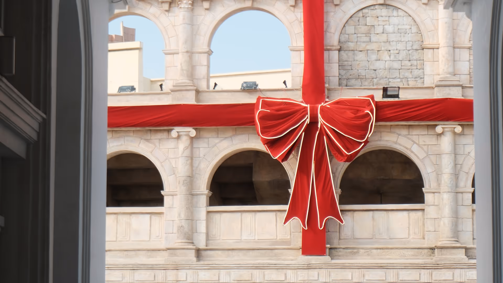 The grand arched facade of a historic Macao building decorated with an oversized red Christmas bow and ribbon.