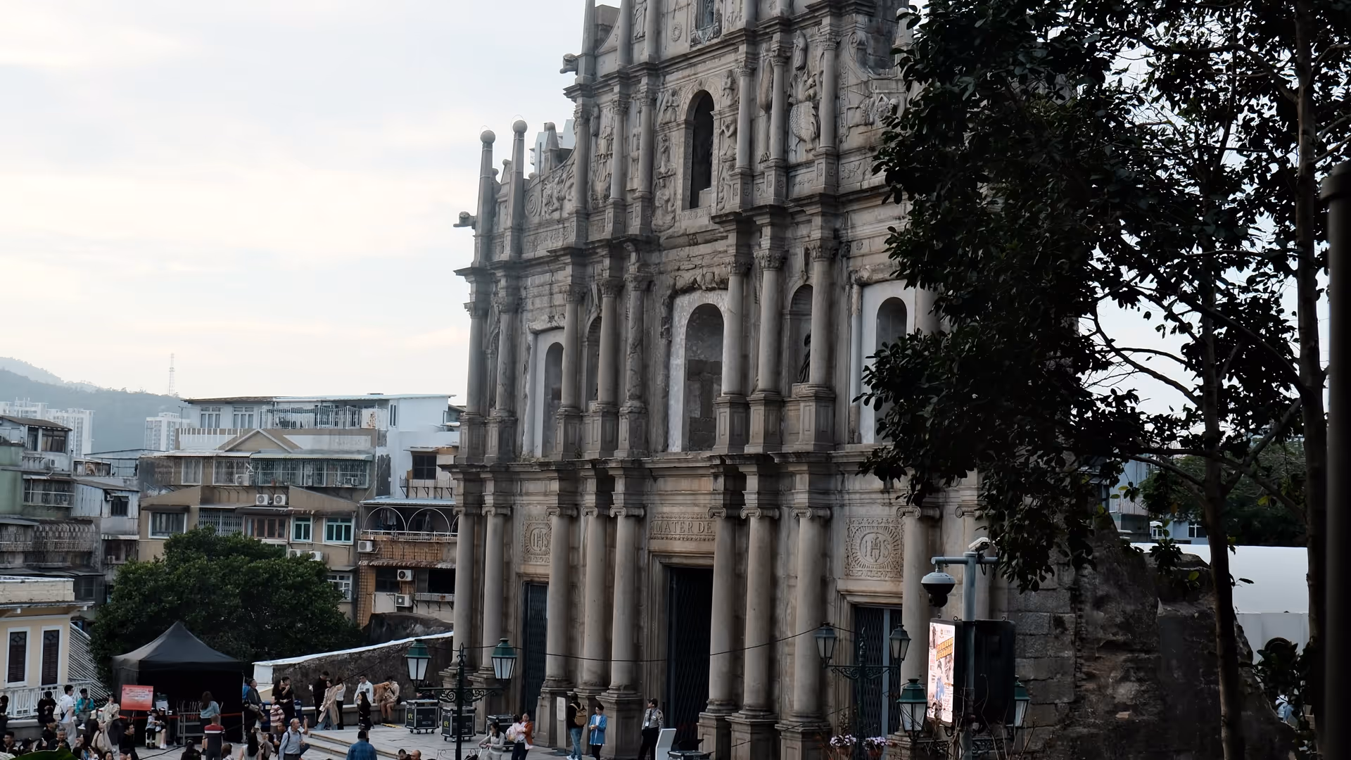 The ornate stone facade of the Ruins of St. Paul rising above the surrounding rooftops and trees in Macao.