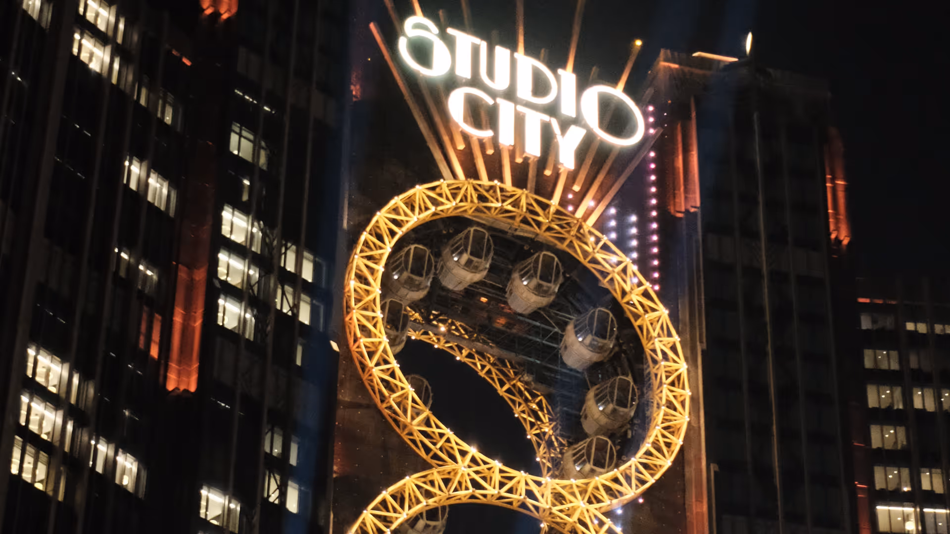The iconic figure-eight Ferris wheel of Studio City Macao glowing gold against a dark night sky.