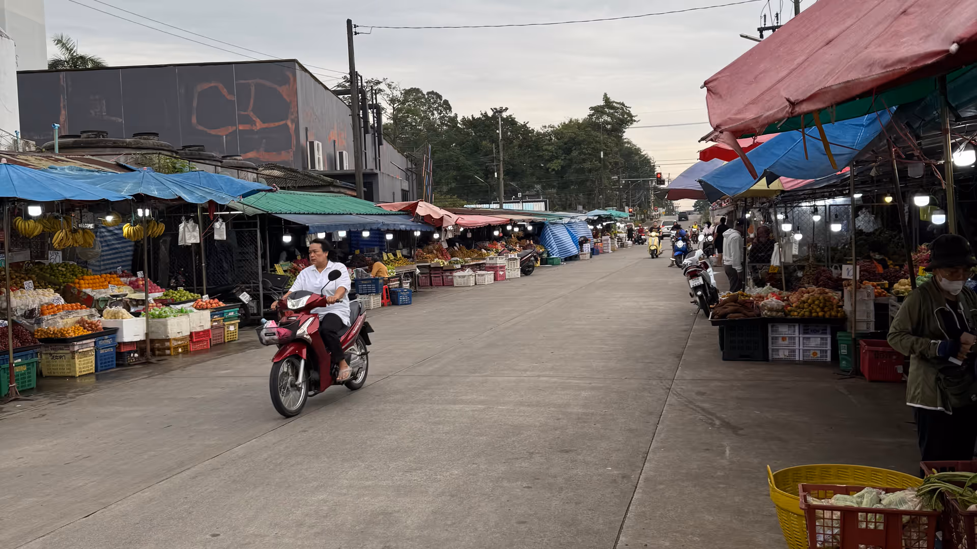 A wide street market in Thailand with vibrant umbrellas and a motorcyclist.