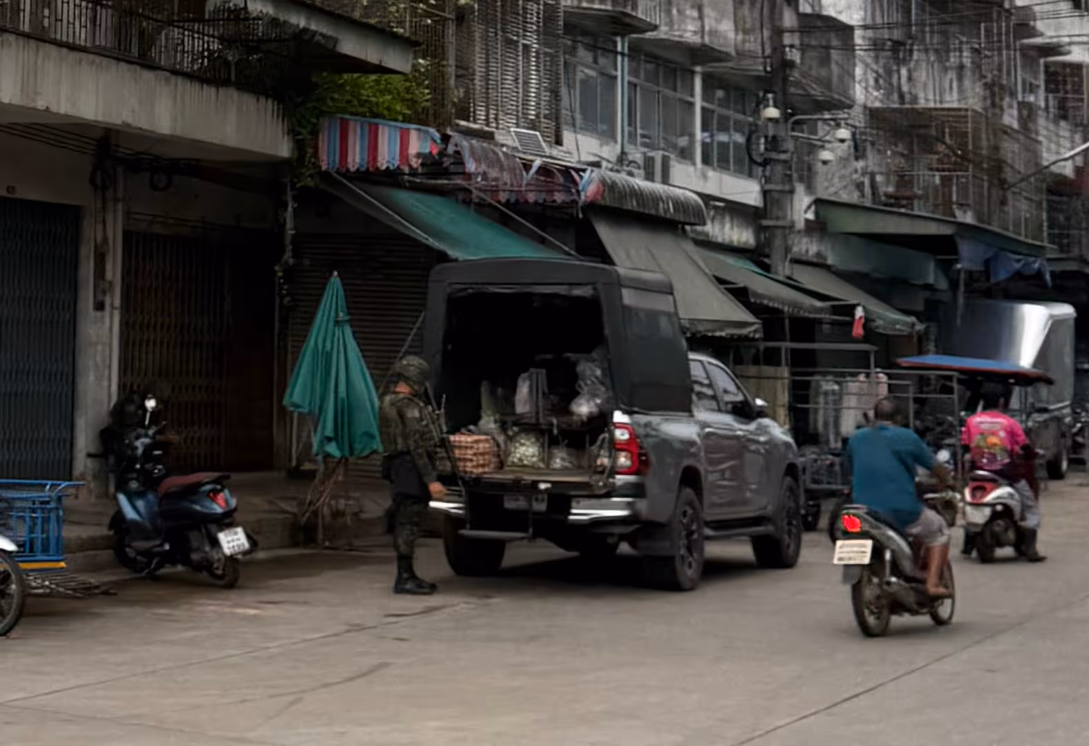 A soldier in full camouflage standing guard near a grey truck on a Narathiwat street.
