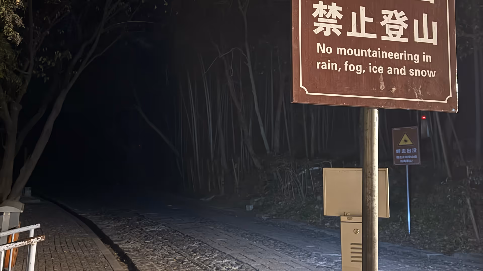 A warning sign at Purple Mountain reading 'No mountaineering in rain, fog, ice and snow', icy stone steps visible behind it.