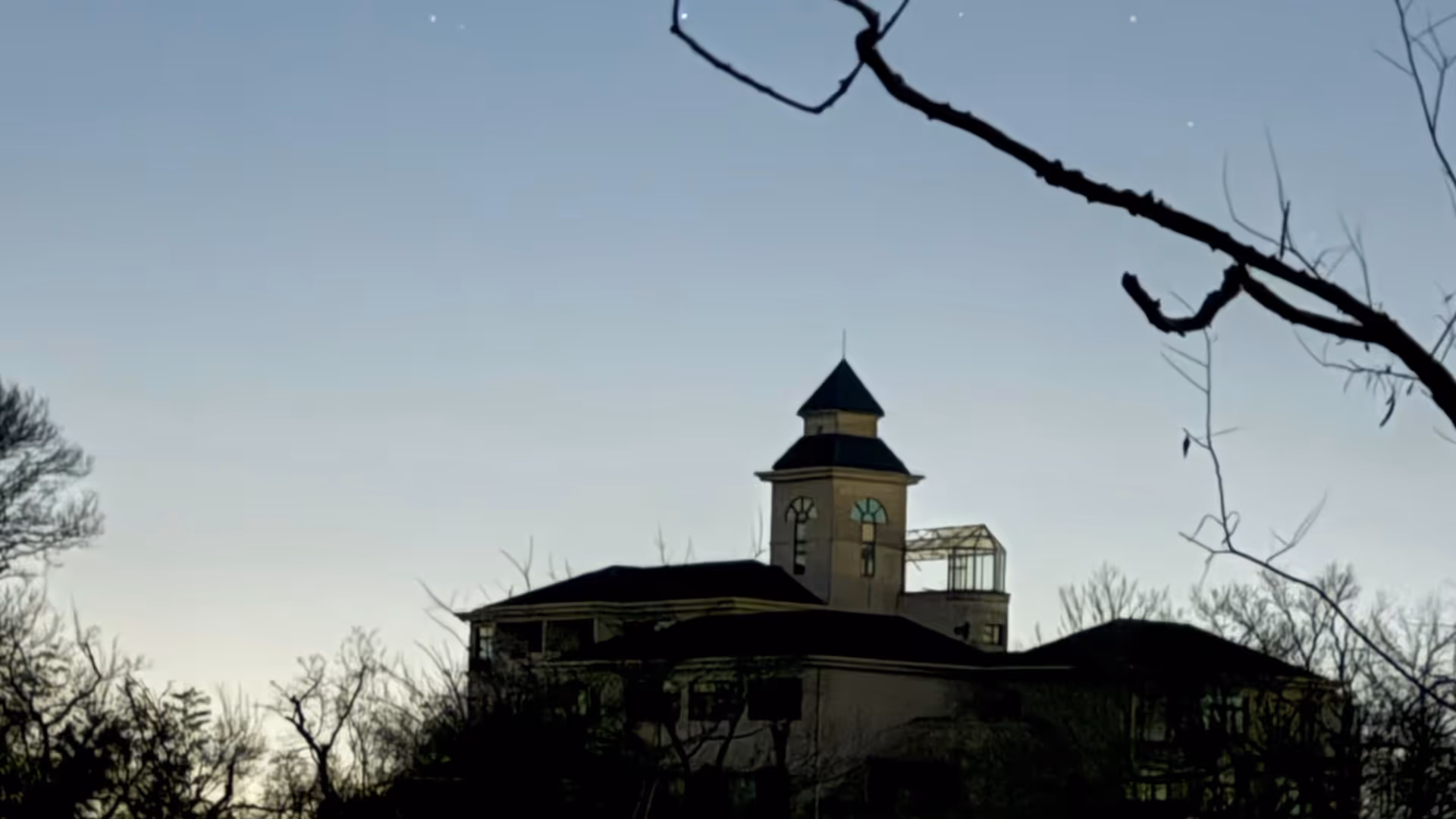An old European-style building silhouetted against a pale dawn sky on Purple Mountain, bare winter branches in the foreground.