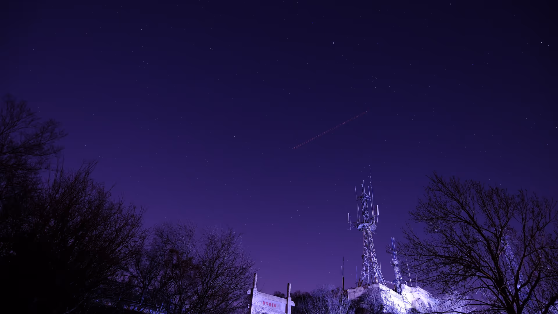 The summit of Purple Mountain at night, a communications tower silhouetted against a deep violet sky with faint stars.