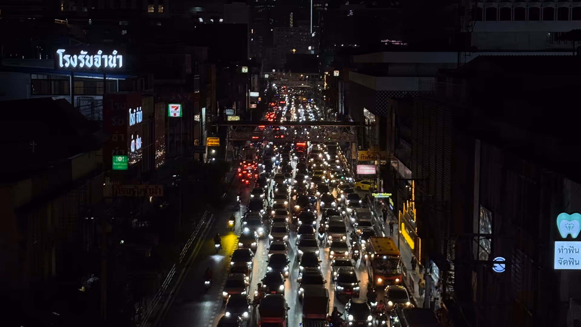 A high-angle night shot of a long line of cars and headlights on a busy Bangkok road.