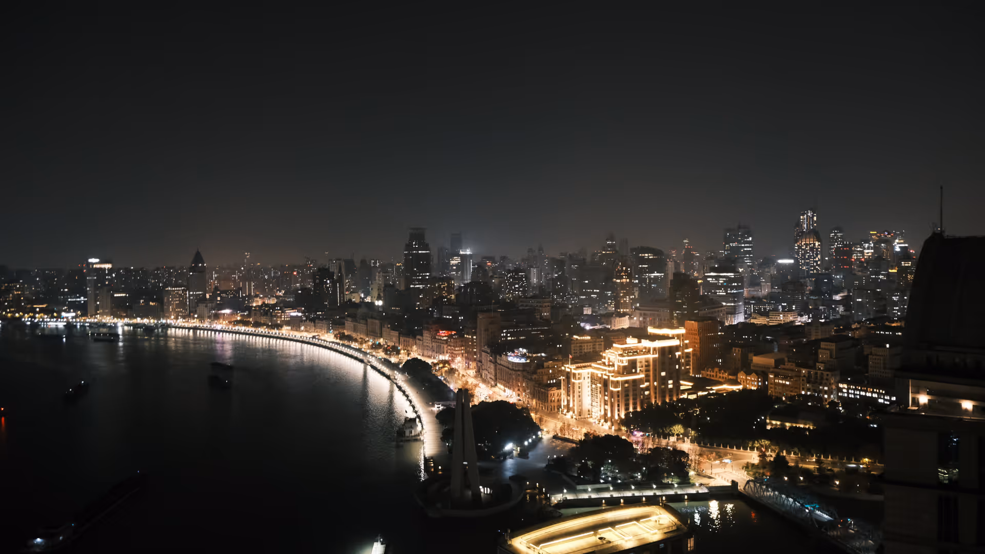 An aerial view of the Bund at night, the Huangpu River curving through the city with the colonial waterfront lit up below.