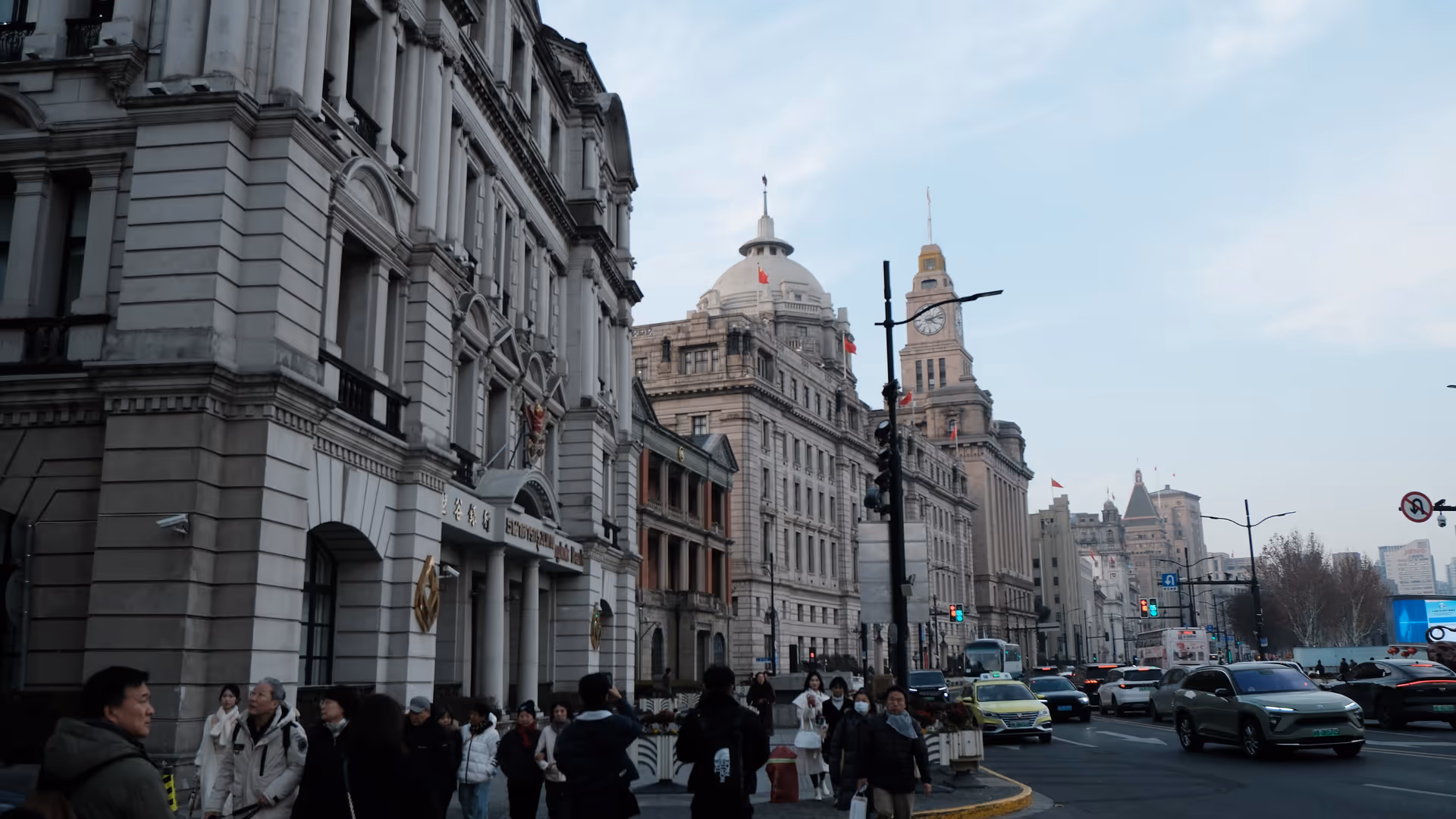 Pedestrians on the Bund street with grand colonial-era buildings stretching into the distance under a clear winter sky.