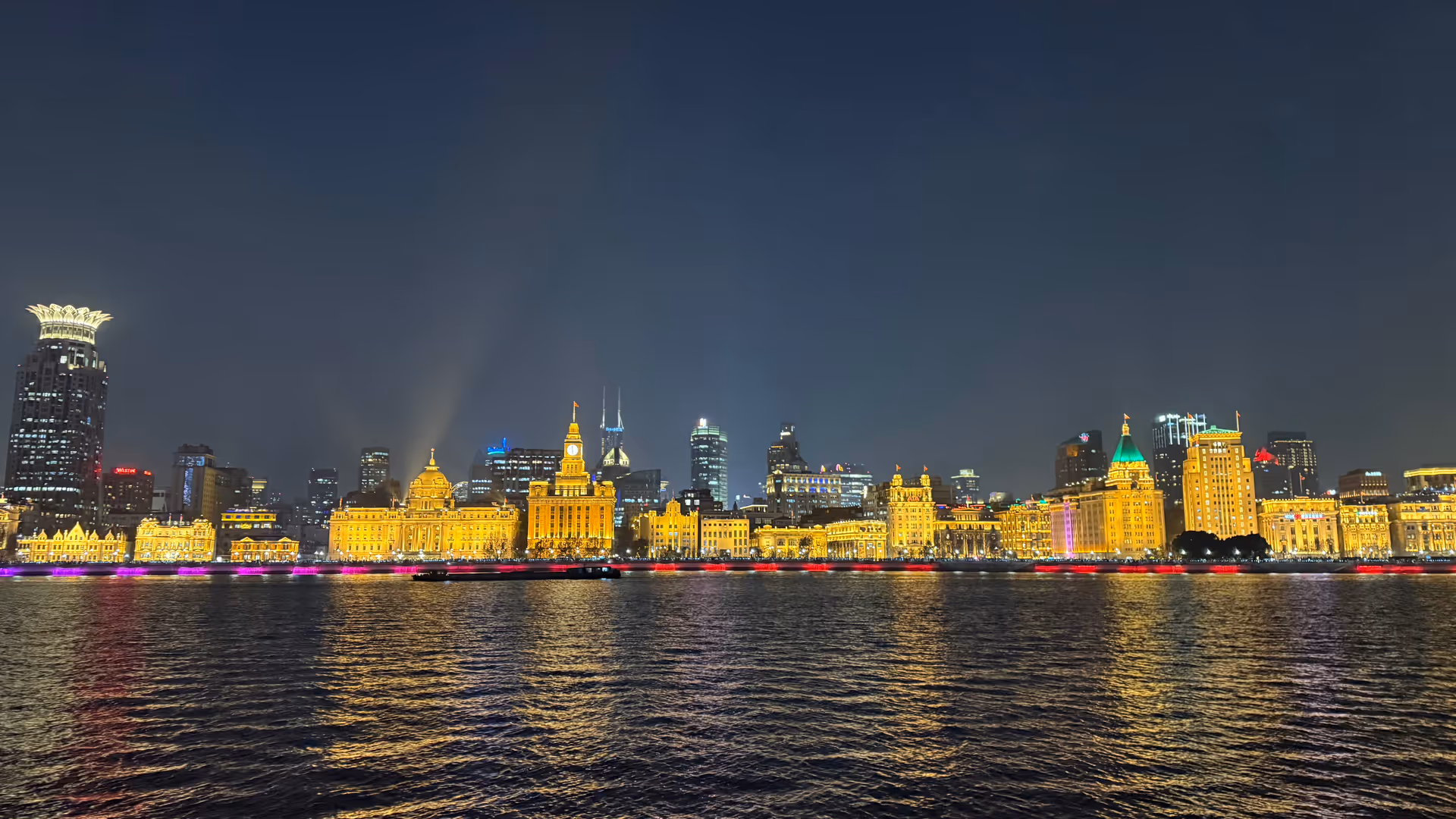 The Bund lit up at night viewed from Pudong, its grand waterfront buildings glowing gold and reflected on the Huangpu River.