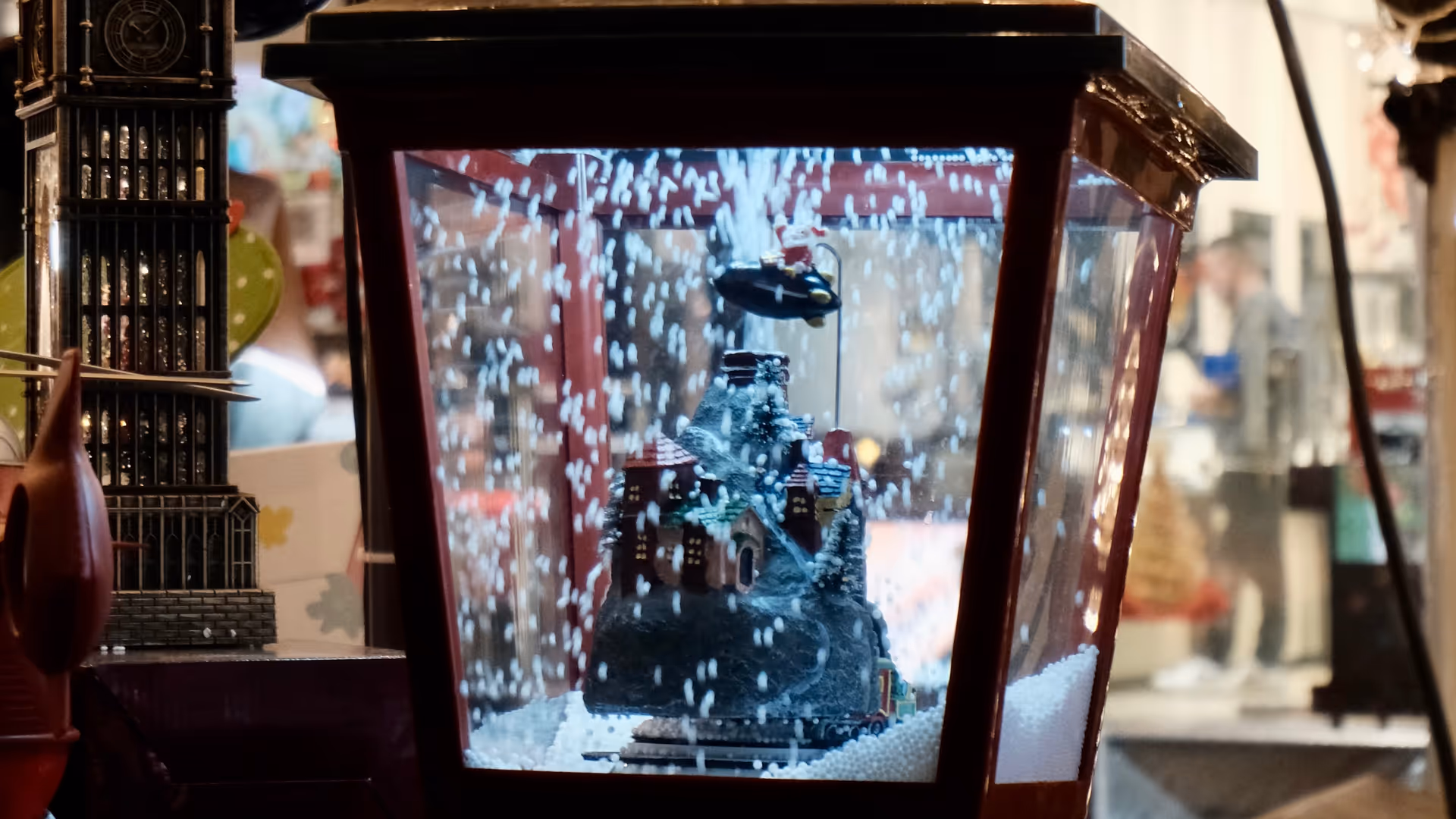 A Christmas lantern with a snow globe scene inside, hanging among decorative baubles at a Shanghai street market.