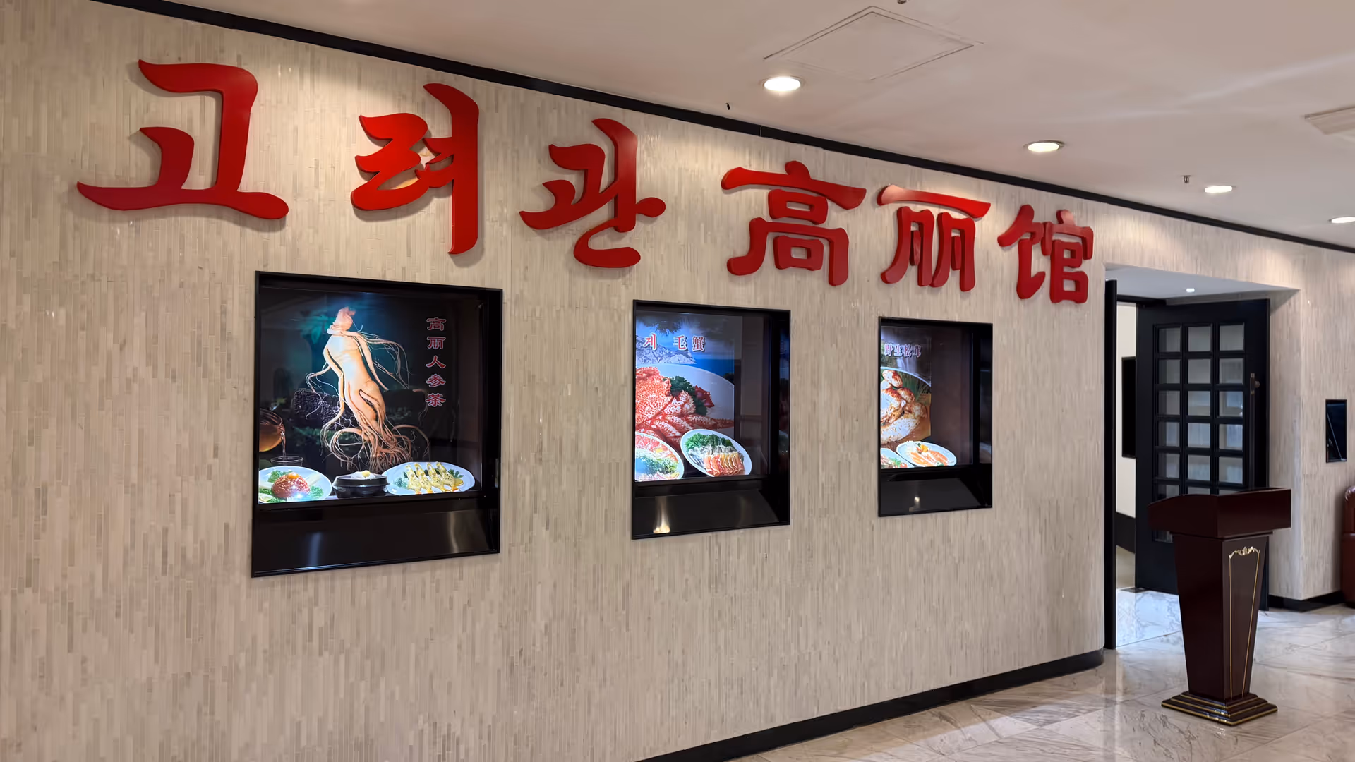 The entrance lobby of a North Korean restaurant in Shanghai, red Korean and Chinese characters on the wall alongside food display photos.