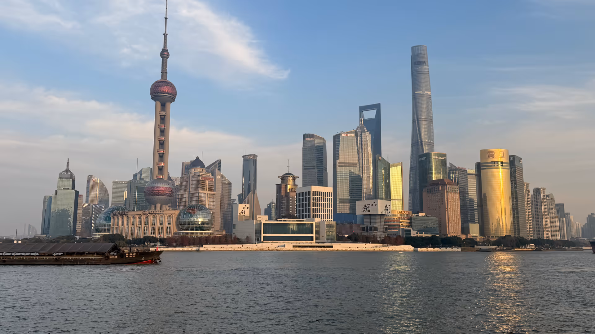 The Pudong skyline across the Huangpu River on a clear winter afternoon, the Oriental Pearl Tower and Shanghai Tower dominating the view.