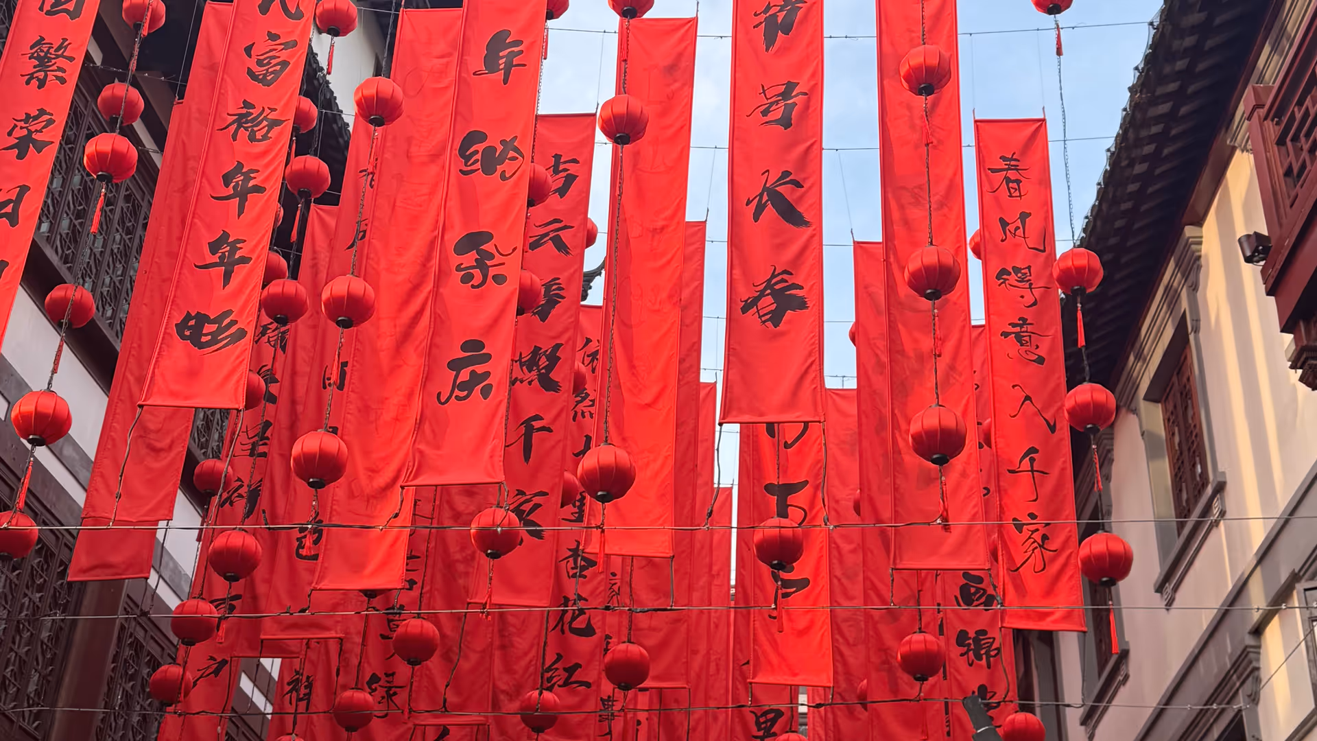 Rows of red calligraphy banners and lanterns hanging between the eaves of Yu Garden's traditional rooftops.