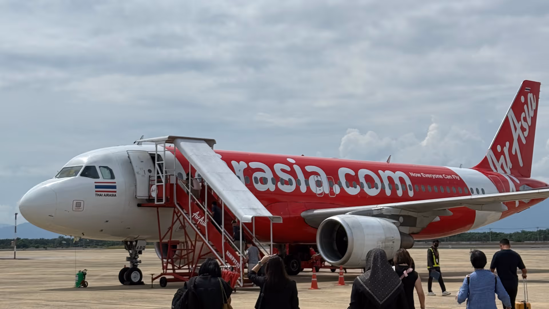 Passengers walking across the tarmac toward a red and white Thai AirAsia plane.