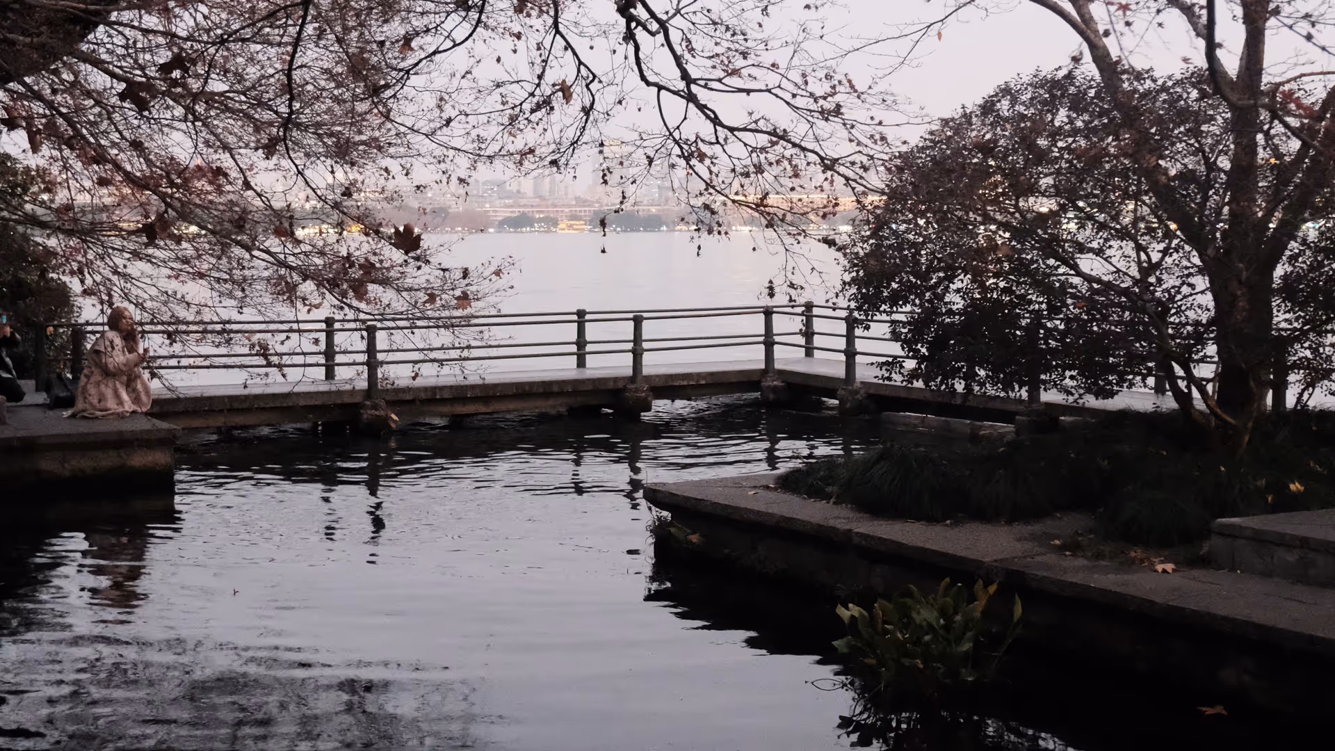 A lakeside pavilion and bare winter trees perfectly reflected in the glassy surface of West Lake at dusk.