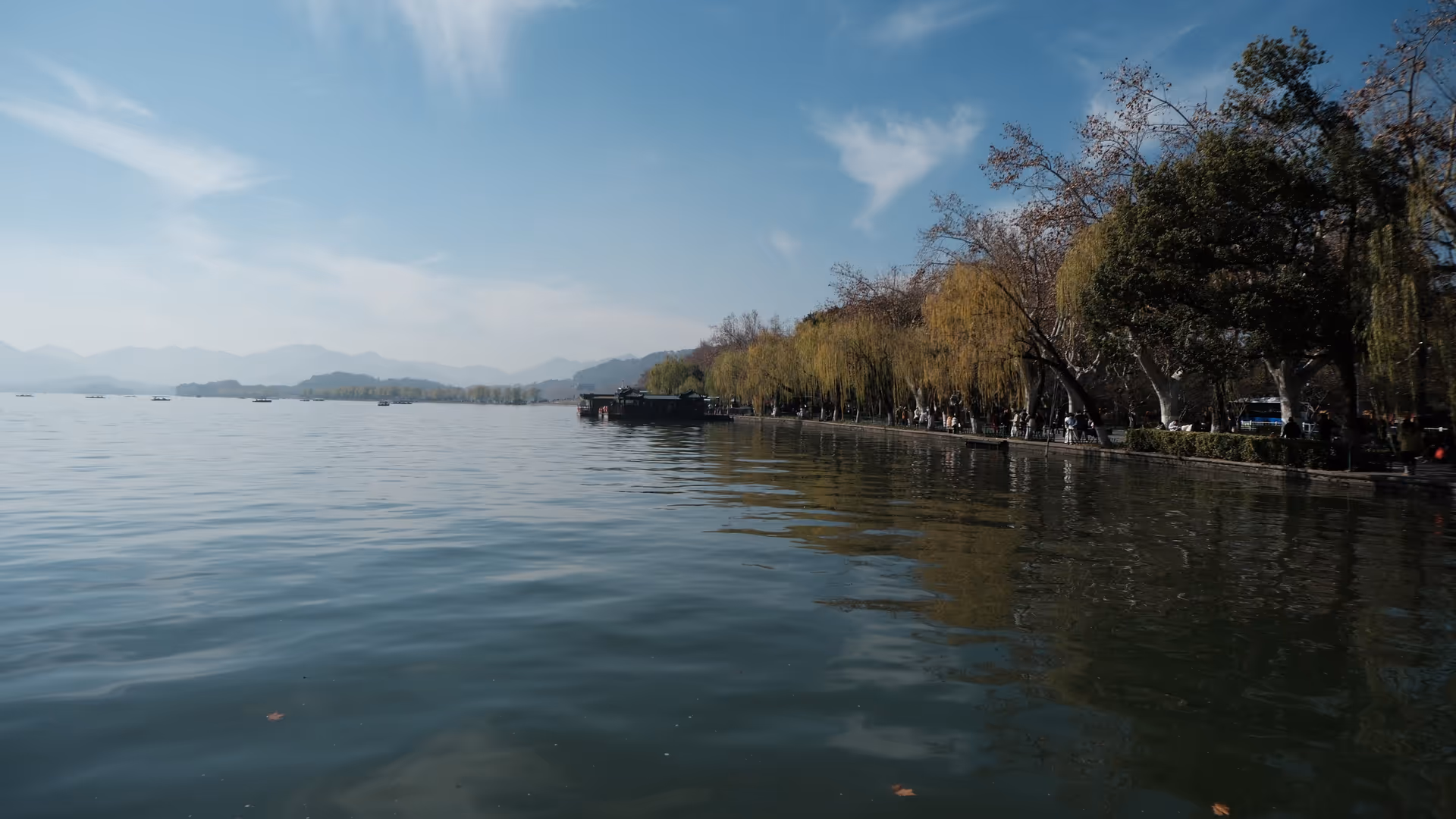 West Lake stretching out under a clear blue winter sky, willows and bare trees lining the calm shoreline.