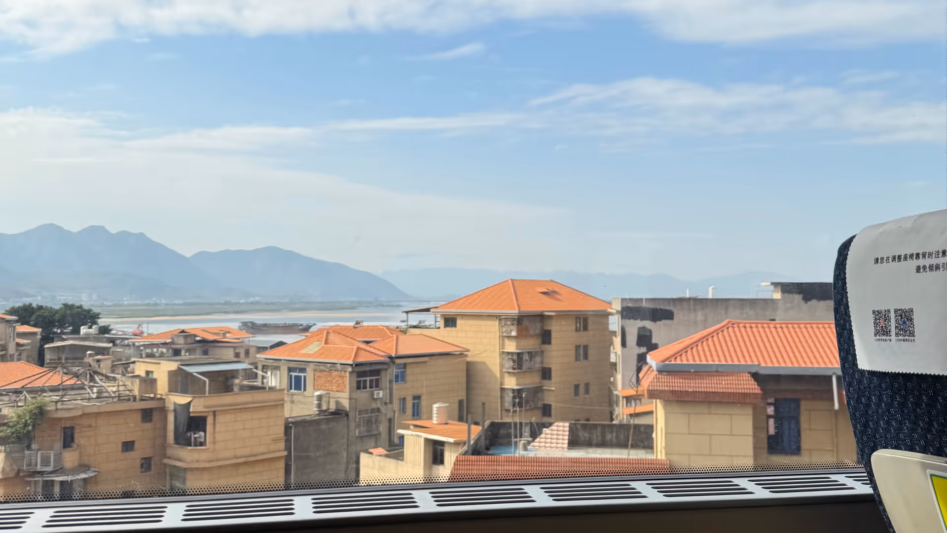 The view from an HSR train window leaving Xiamen, terracotta-roofed buildings and the sea visible in the distance.