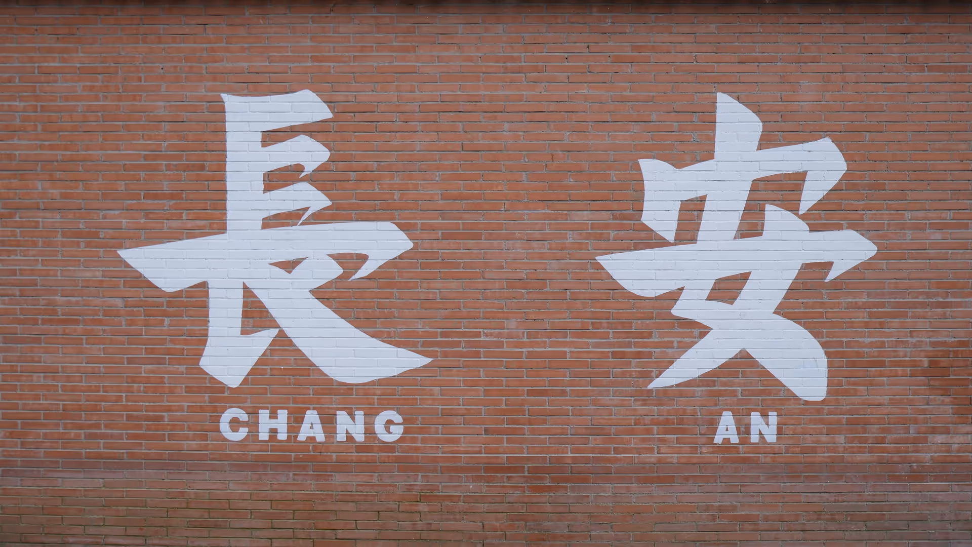 Large white Chinese characters reading Chang An painted on a red brick wall.