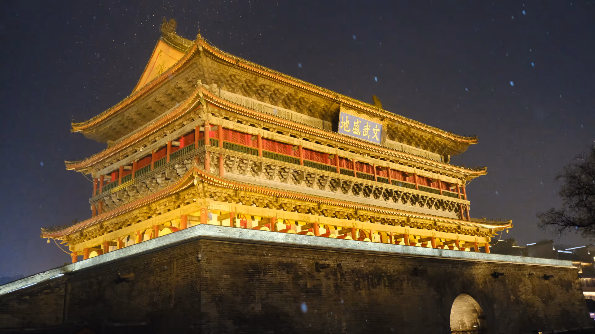 The Xi'an Drum Tower glowing gold against a dark snowy night sky, snowflakes visible in the air.