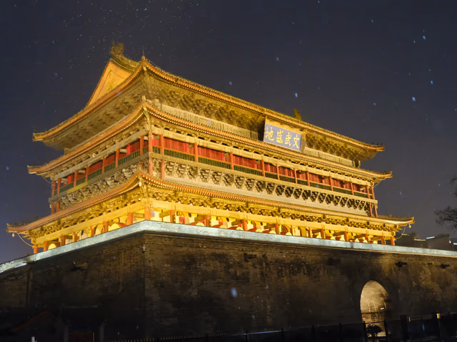 The Xi'an Drum Tower glowing gold against a dark snowy night sky, snowflakes visible in the air.