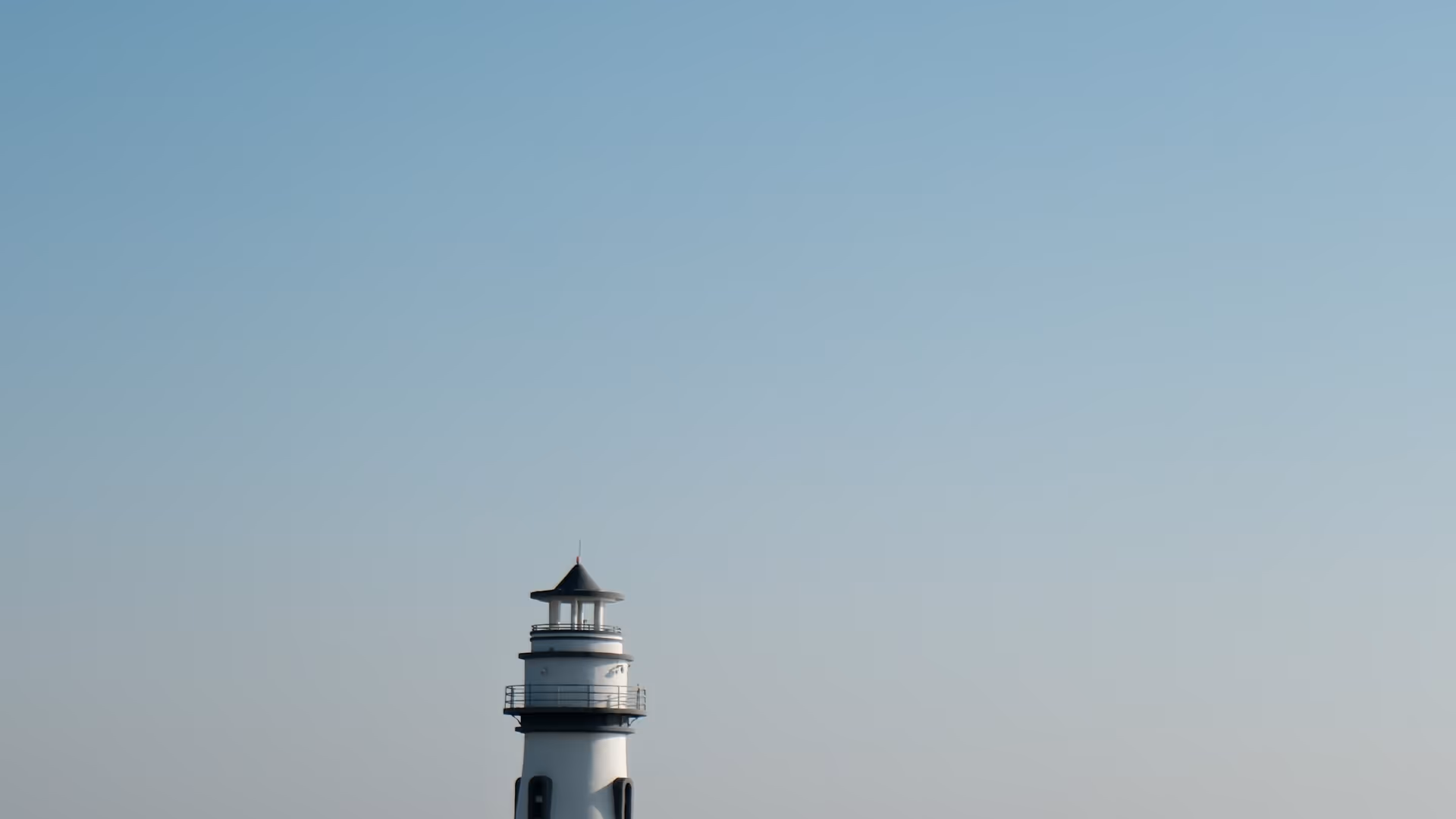 A small white lighthouse standing alone at the edge of the sea on a clear, hazy morning in Zhuhai.